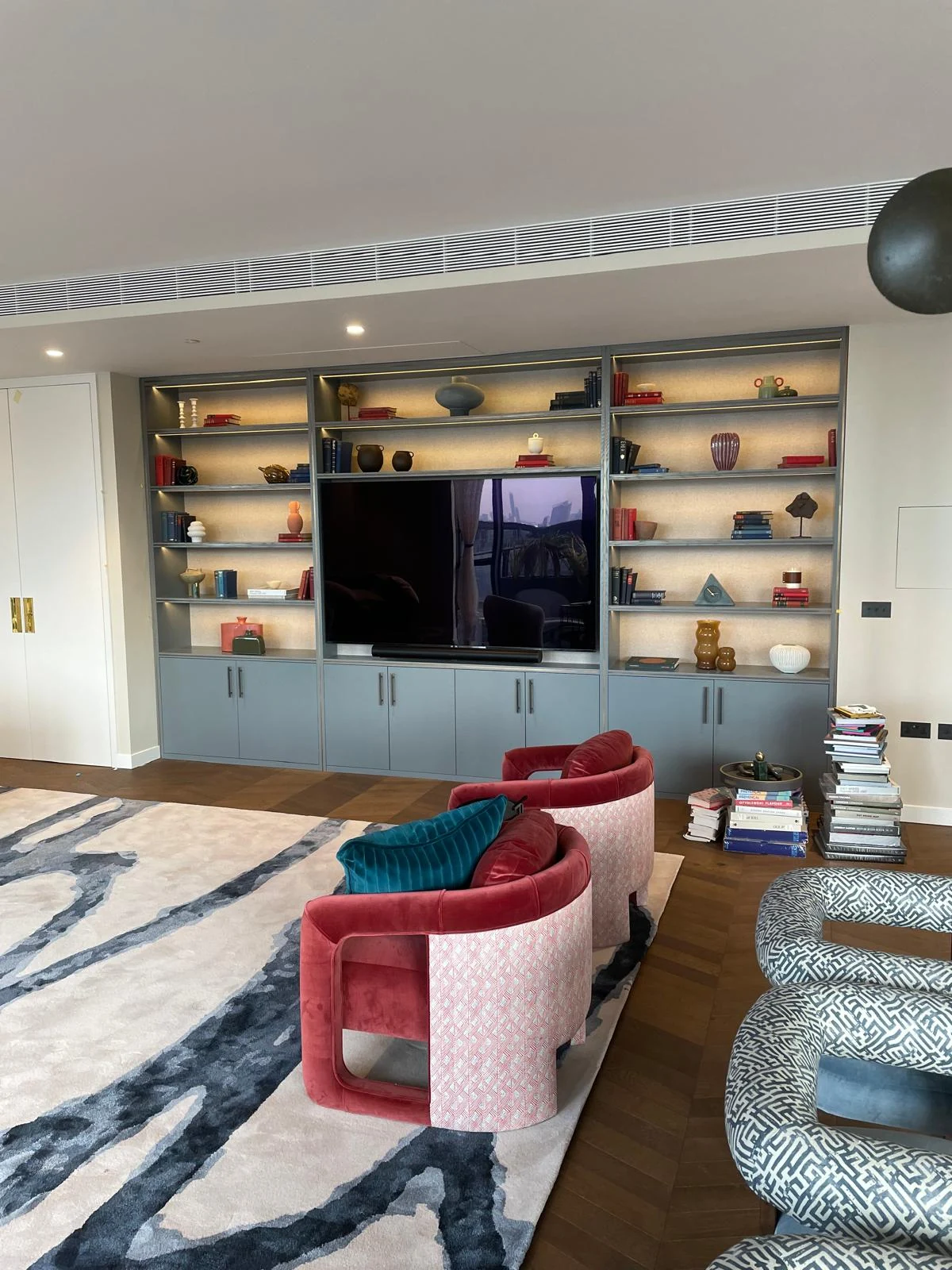Blue-grey media wall seen across a living room with red accent chairs.