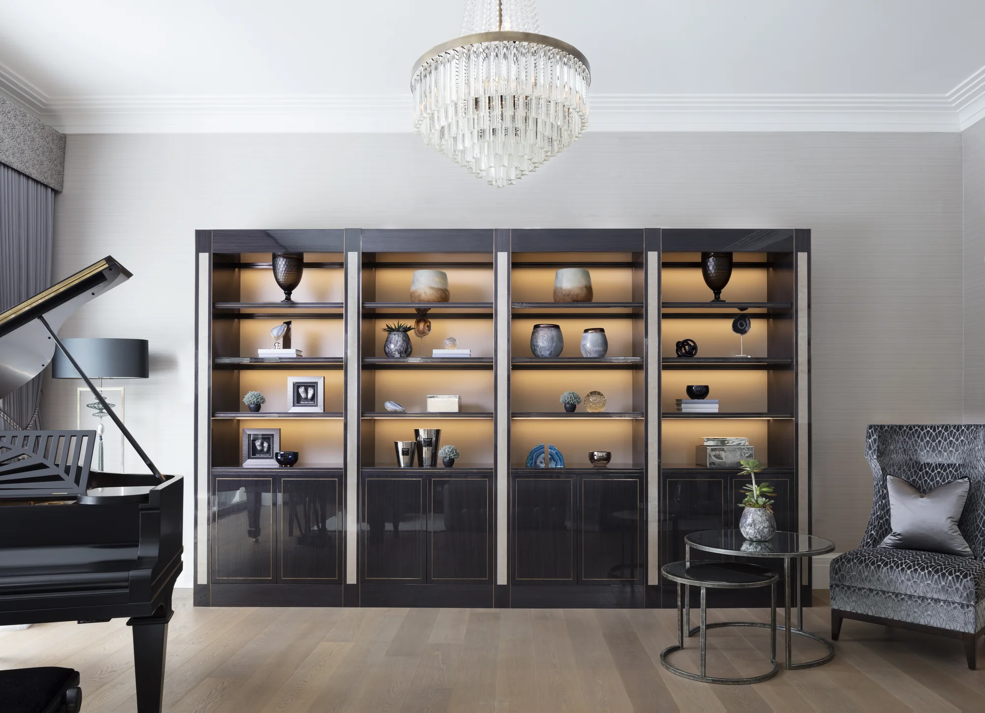 Full-width fitted display bookcase with lighting beside a grand piano