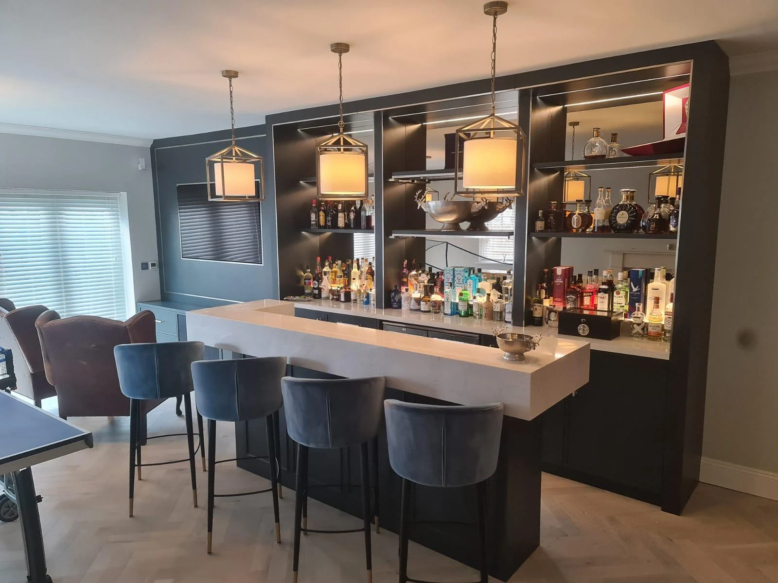 Three-quarter view of the home bar with illuminated bottle display and pendant lights.