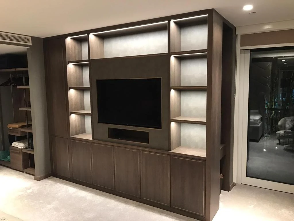 Brown fitted media unit with lit side niches, television opening and base cupboards.