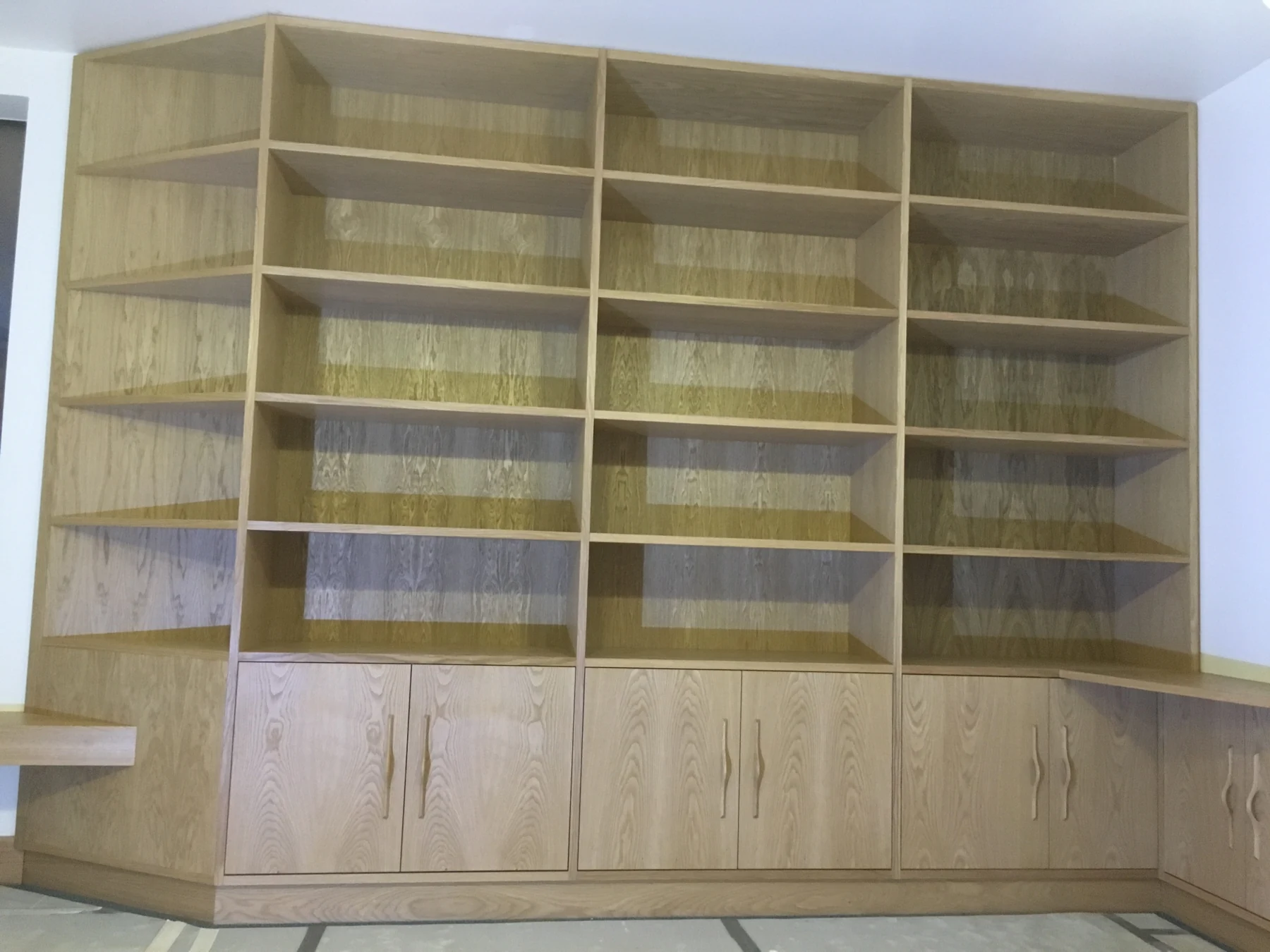 Light wood-grain corner library with tall shelves and low cupboards.