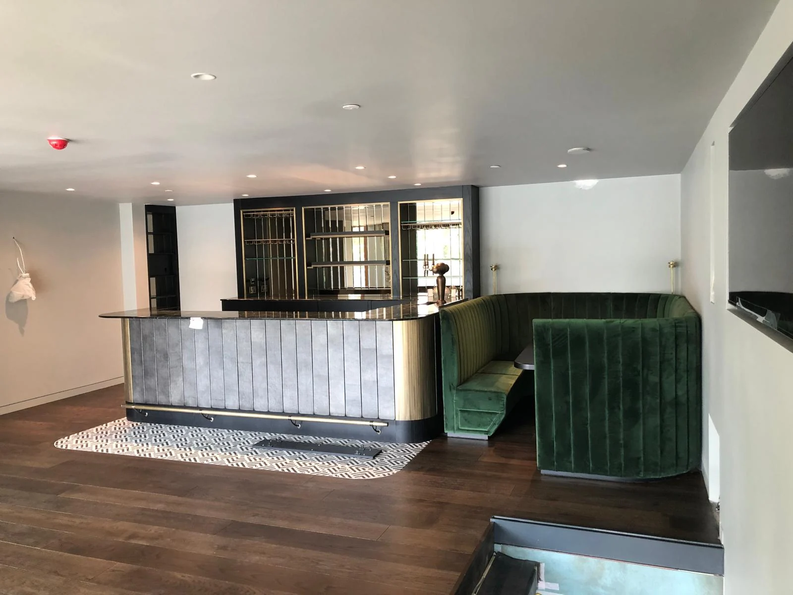 Wide room view of a curved bar counter beside a green upholstered seating nook.