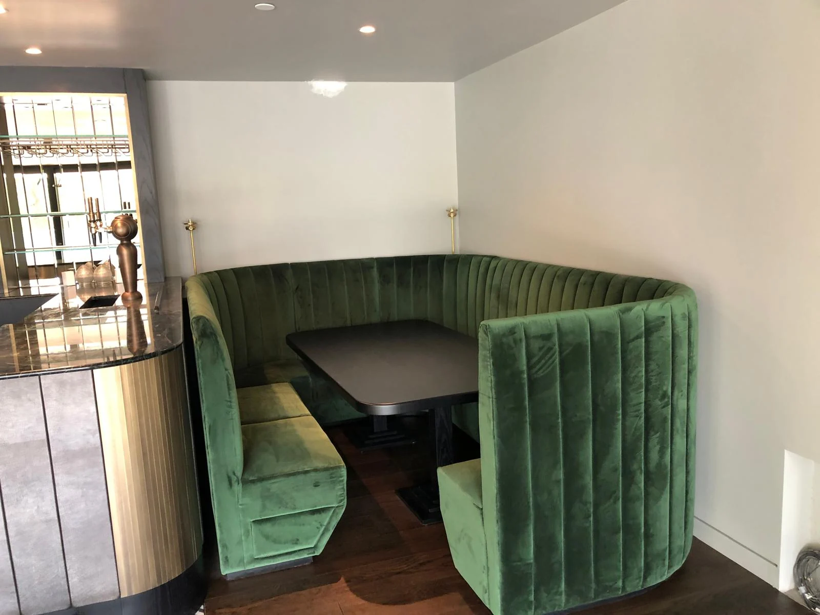 Curved green banquette seating and a dark table beside the bar.