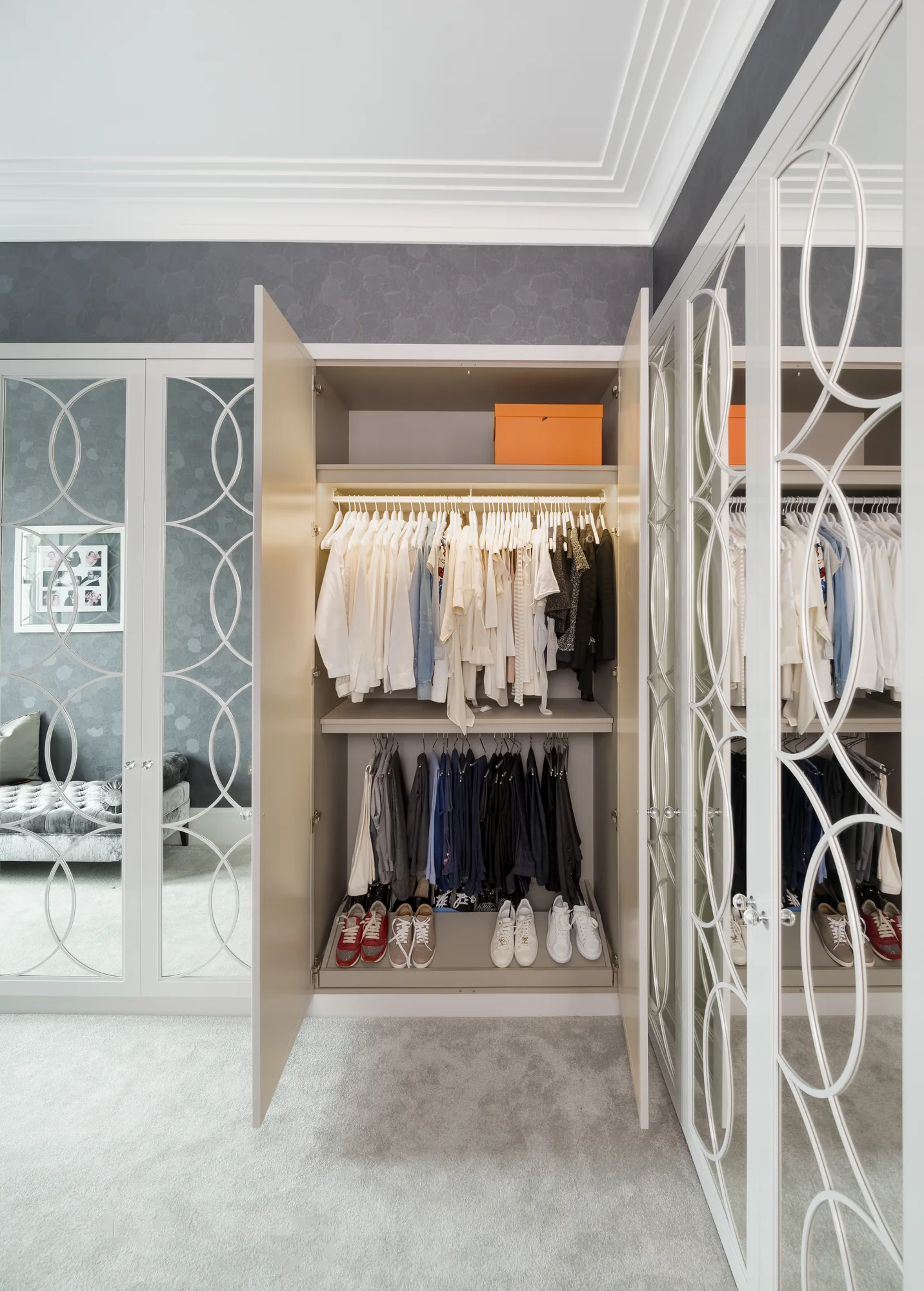 Open mirrored wardrobe revealing hanging clothes, an upper shelf and lower storage