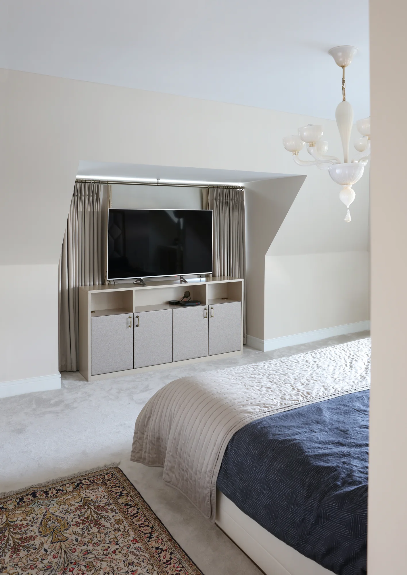 Bedroom TV cabinet beneath a sloping ceiling with open shelves and pale lower cupboards