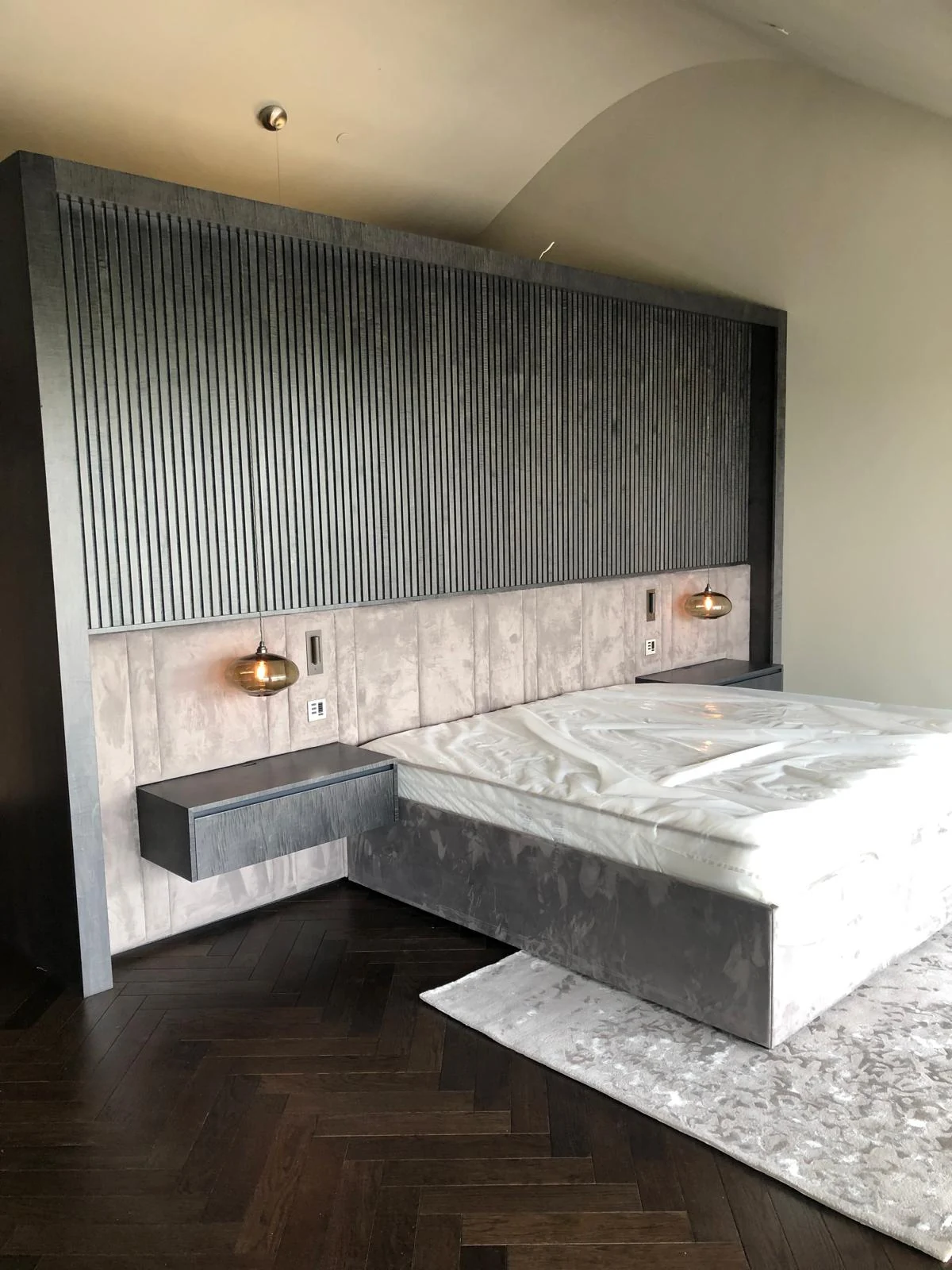 Bed wall with vertical fluting, padded panels, floating bedside units and wall lights.