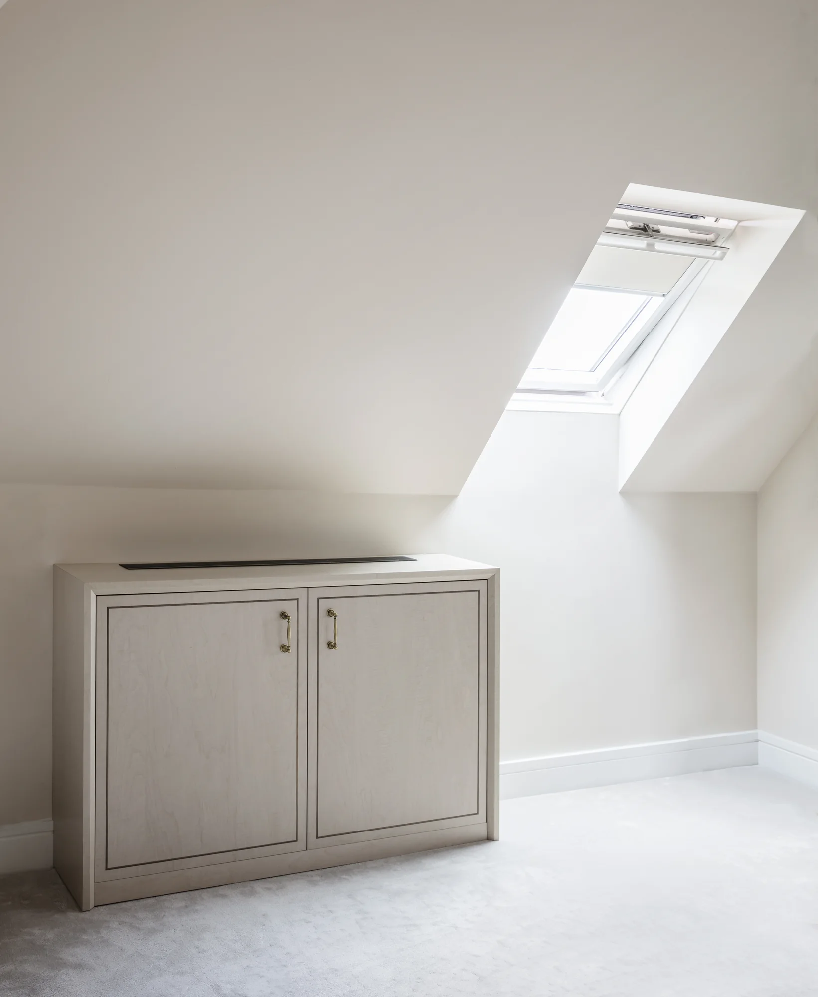 Low pale cabinet beneath a rooflight with framed doors and a ventilation grille in the top