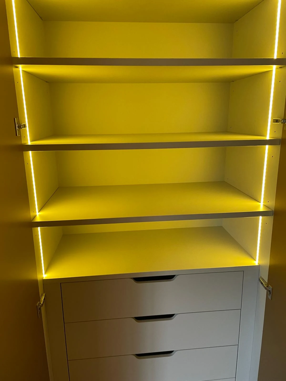 Open gold-tone cabinet revealing bright shelves, concealed lighting and lower drawers.