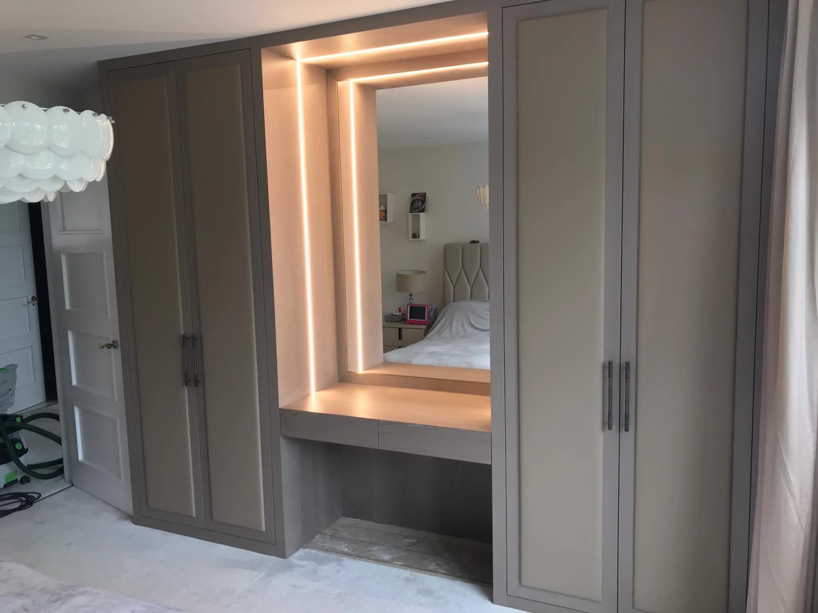 Grey fitted wardrobes around a mirror and warmly lit dressing recess.