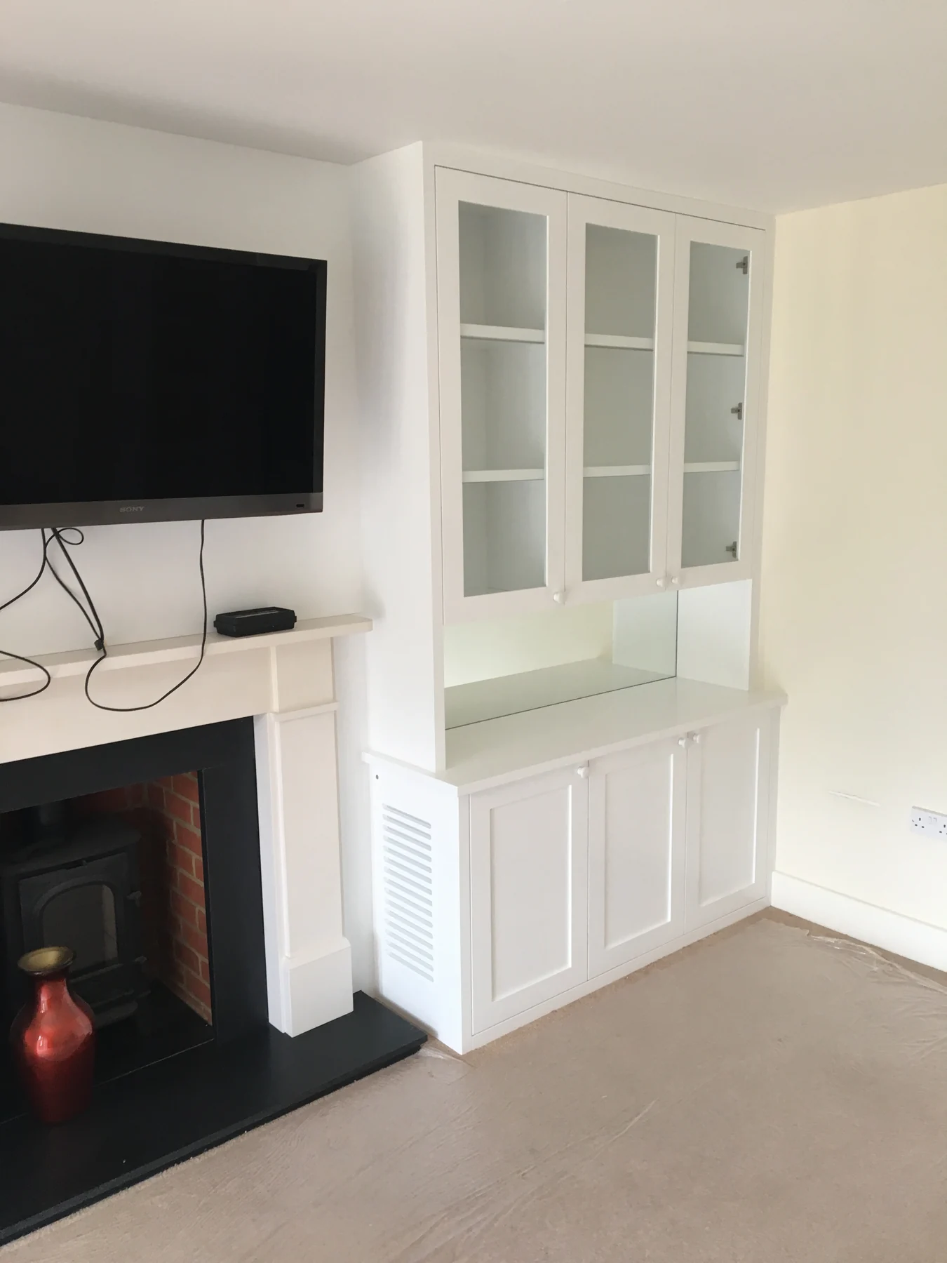 White glazed alcove cabinet and lower panelled cupboards beside a fireplace.