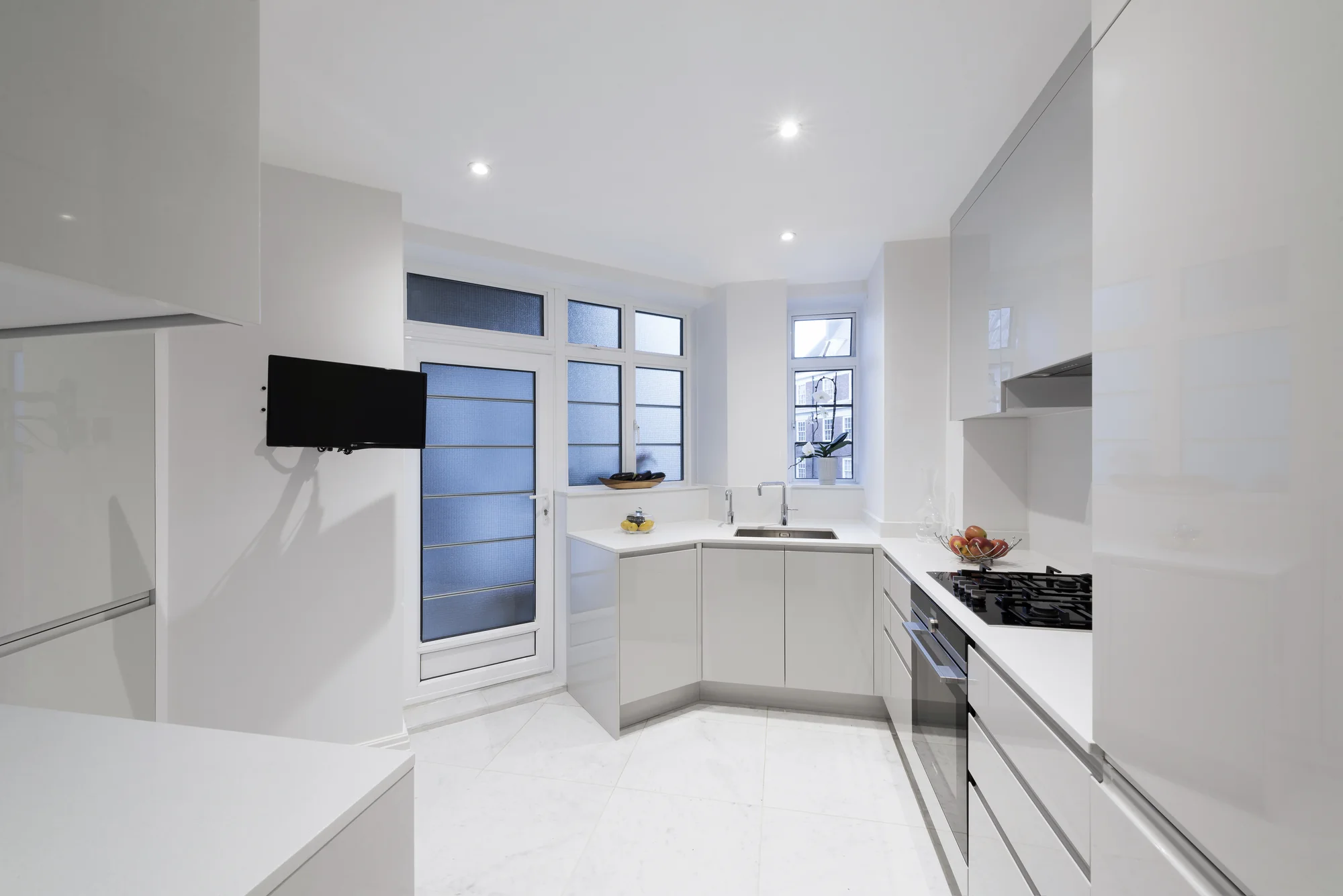 White handleless fitted kitchen with a cooking run, sink and tall storage